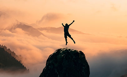 Man with arms outstrethched in victory in the mountains with a warm orange sky