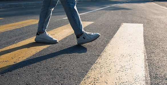 Man in comfortable shoes and jeans walking in a crosswalk. We see only legs and feet below the knees
