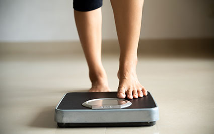 Woman stepping onto a scale. We see her ankles and the bottom of her pants