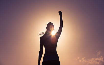 Woman in shadow against light, with her arm raised in confidence