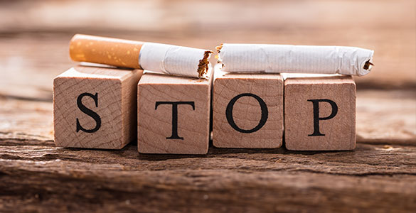 Cigarette on top of wood block letters that spell STOP. Wood background,
