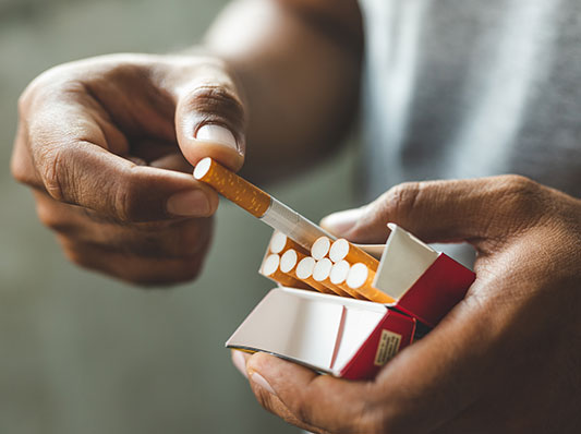 Man pulling a cigarette out of a pack, focus on filters