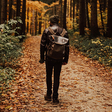 Man with a backpack walking through wooded area with leags on the ground