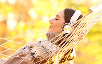 Woman laying in hammock wearing headphones with eyes closed