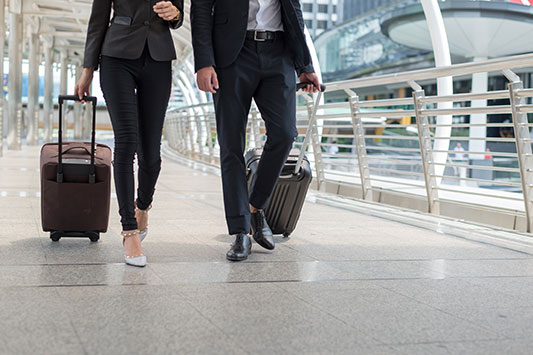 Man and woman walking through an airport pulling luggage behind them.