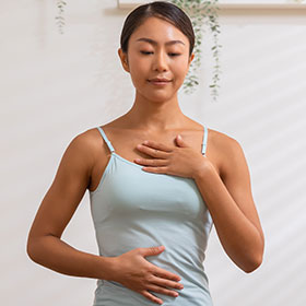 Young woman with a hand on her chest and a hand on her abdomen doing breathing exercises
