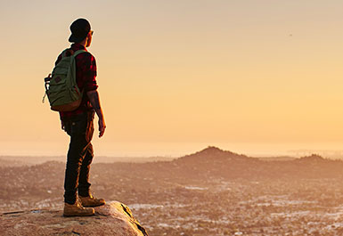 Man staring out at sunset after hike. Sky is yellow orange.